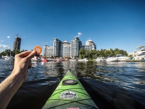 person holding green kayak on water near city buildings during daytime