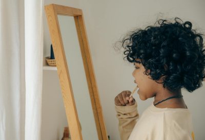 Young child with curly hair brushing teeth in front of mirror, emphasizing morning routine and hygiene.
