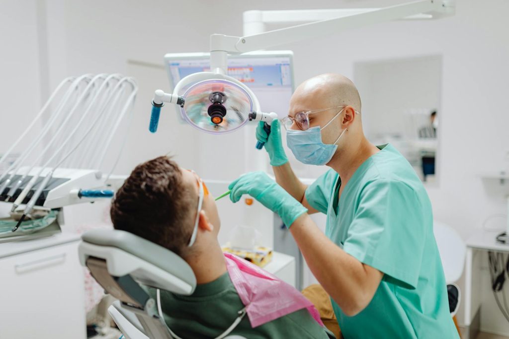 A dentist in a medical clinic conducts a dental check-up on a seated patient.