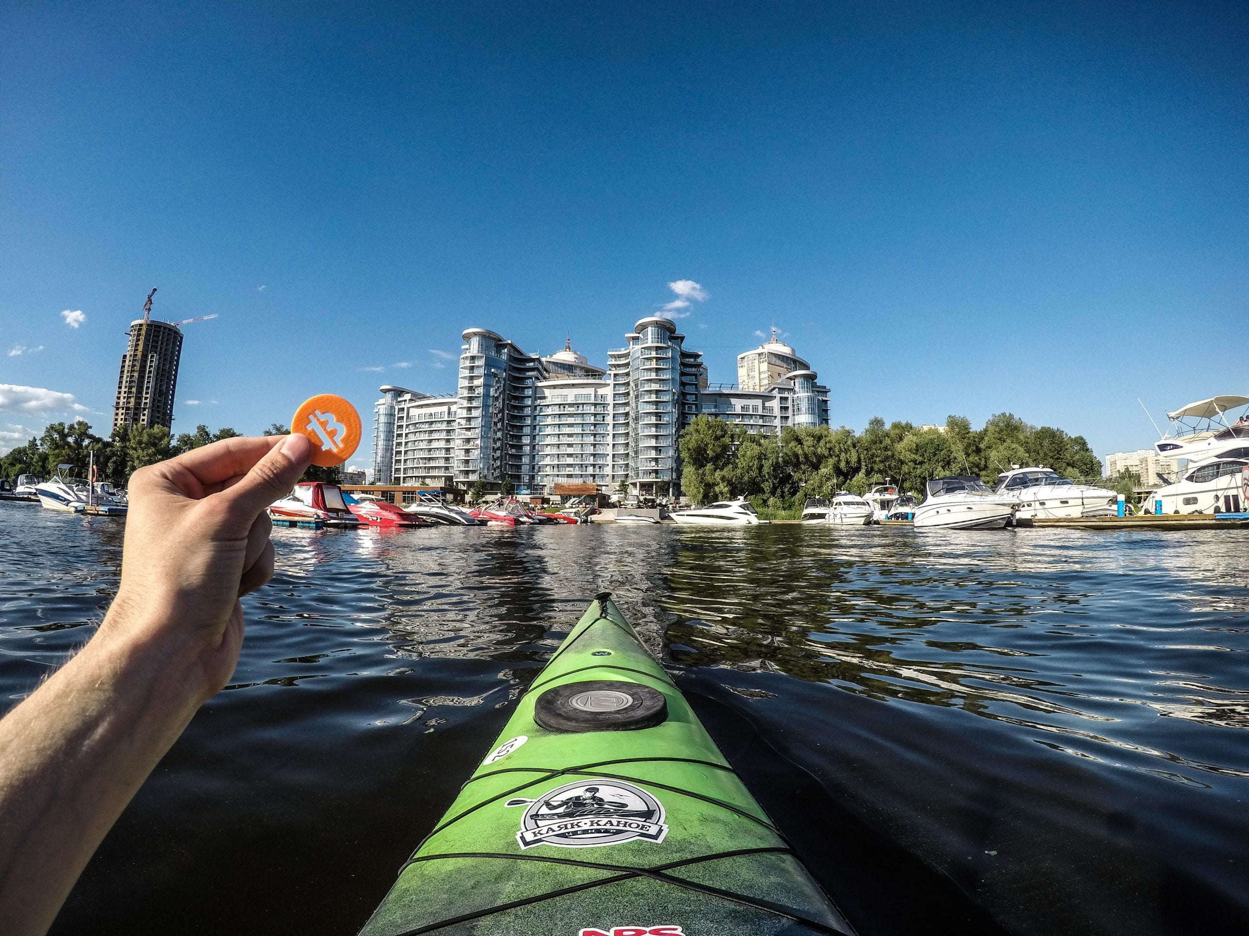 Cities Around the Globe which are Turning Up as “Bitcoin Hotspots” person holding green kayak on water near city buildings during daytime