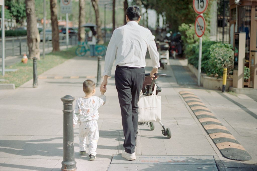 A father walks with his child down the sidewalk.